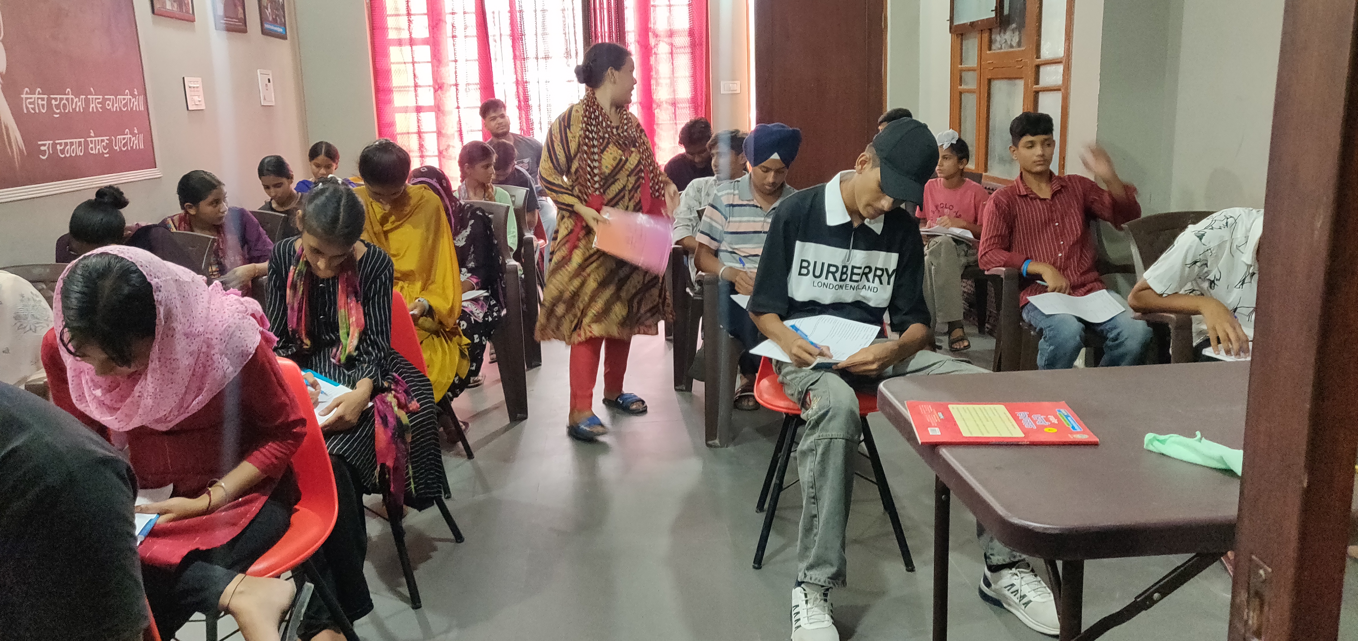 A young Punjabi student reading in a bright, modern village library with bookshelves and large windows